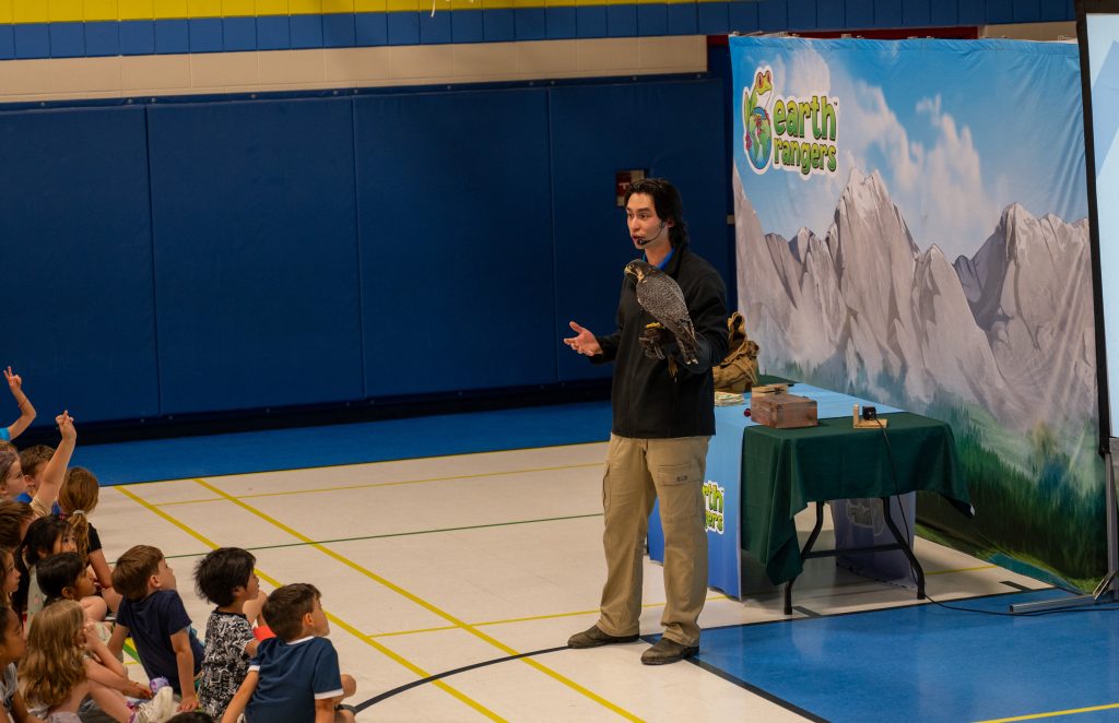 Man holds falcon at a school assembly.