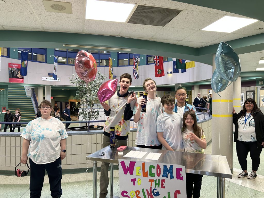 Students pose with balloons at a sign-in table for a school dance.