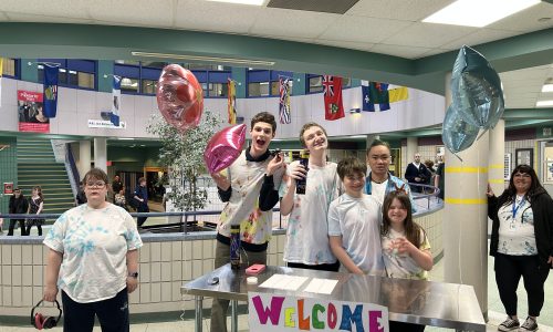 Students pose with balloons at a sign-in table for a school dance.