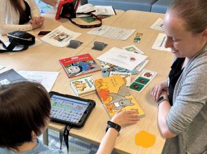 Child and adult read a book together while using a communication device.