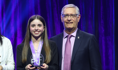 Student stands with an adult while holding an award at a ceremony.