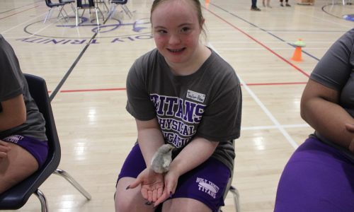 Student holds a bird while attending an event in a school gym.