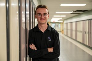 Male student poses leaning against a locker in a school.