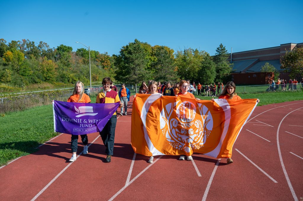 Students carry banners and walk around a track at a school.