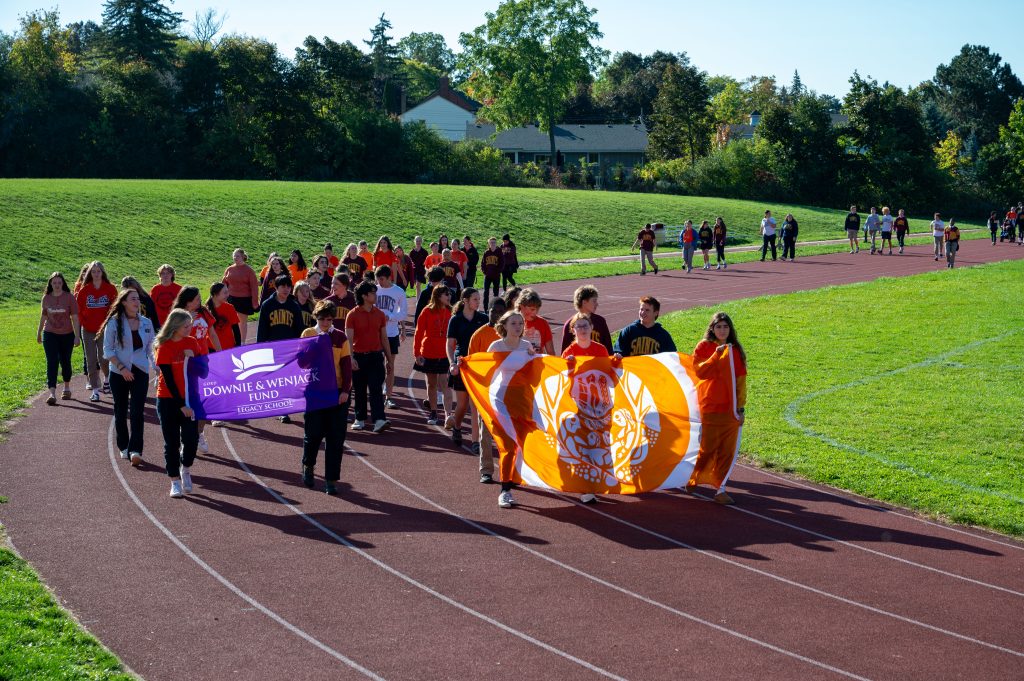 Students carry banners and walk around a track at a school.