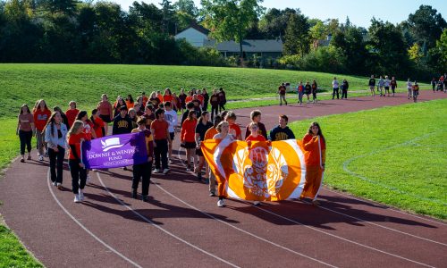 Students carry banners and walk around a track at a school.