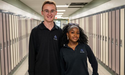 Two students pose together in a hallway at a school.