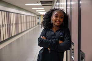 Female student poses leaning against a locker in a school.