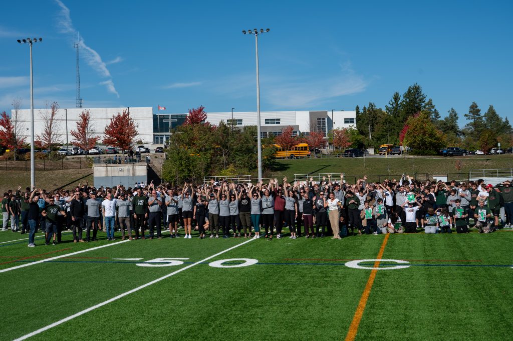 Large group photo of students and staff on a football field at a school.