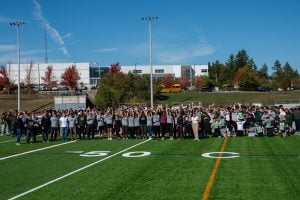 Large group photo of students and staff on a football field at a school.