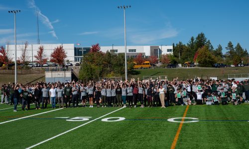 Large group photo of students and staff on a football field at a school.