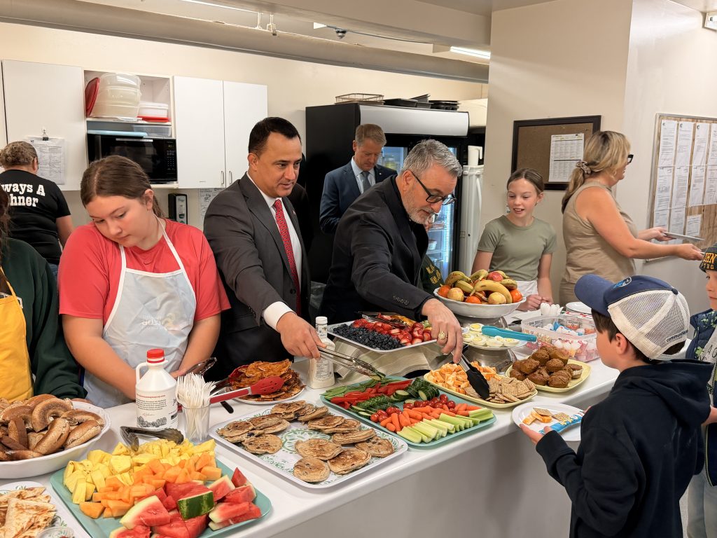 Two adults serve meals to students at a breakfast program.