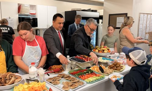 Two adults serve meals to students at a breakfast program.