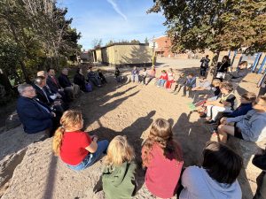 A large group sits in a circle outside of a school.