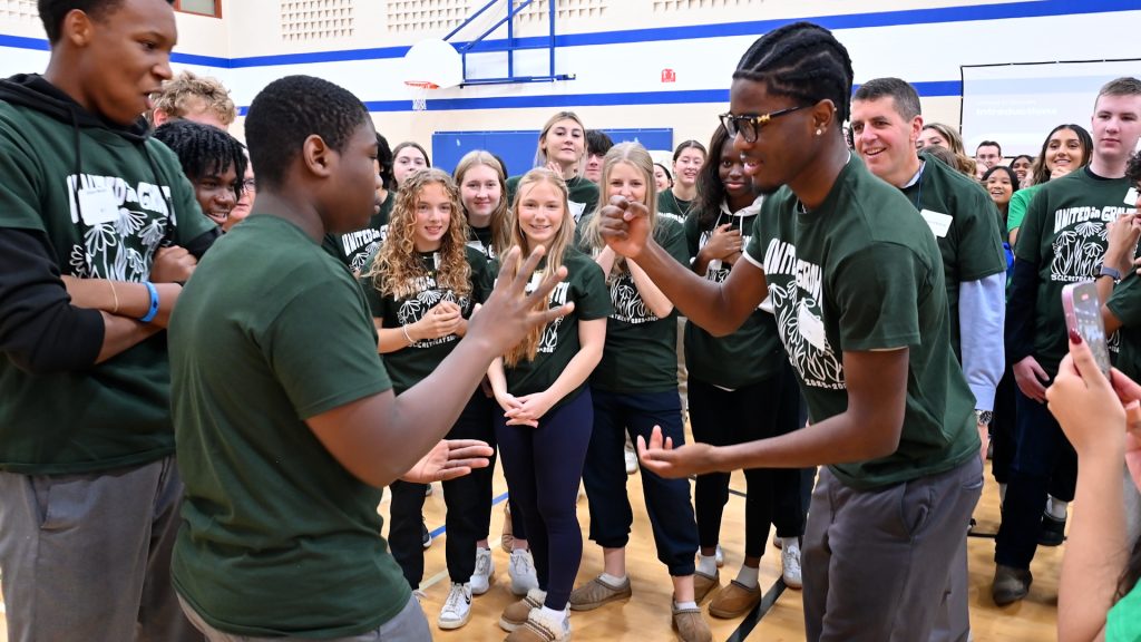 Two students play Rock, Paper, Scissors while a group of students watches.