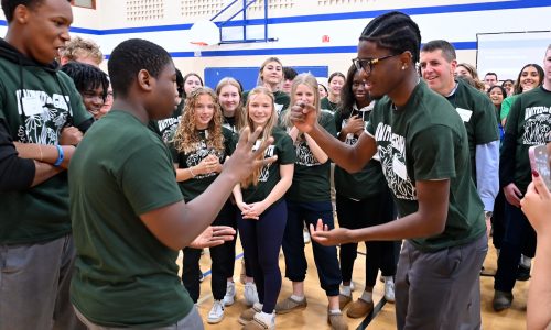 Two students play Rock, Paper, Scissors while a group of students watches.