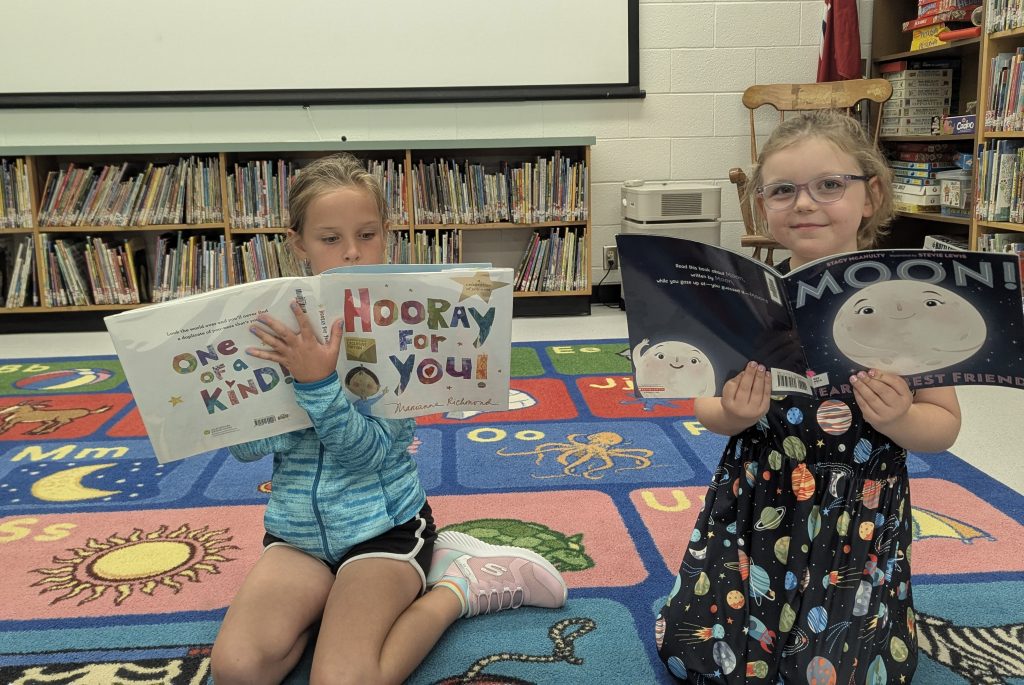 Two young students reading books while sitting in a school library.