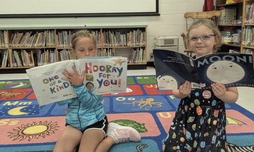 Two young students reading books while sitting in a school library.