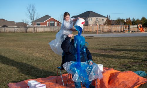 A student dumps a bucket of blue slime on an adult at a celebration at a playground.