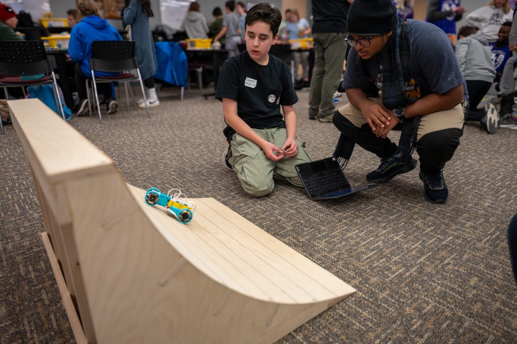 Students attempt to power a small robot built out of Lego up a ramp for a competition.