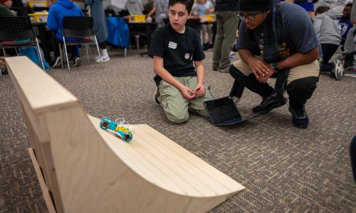 Students attempt to power a small robot built out of Lego up a ramp for a competition.
