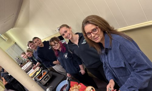 Students and staff members line a table where they prepare food for a community gathering.