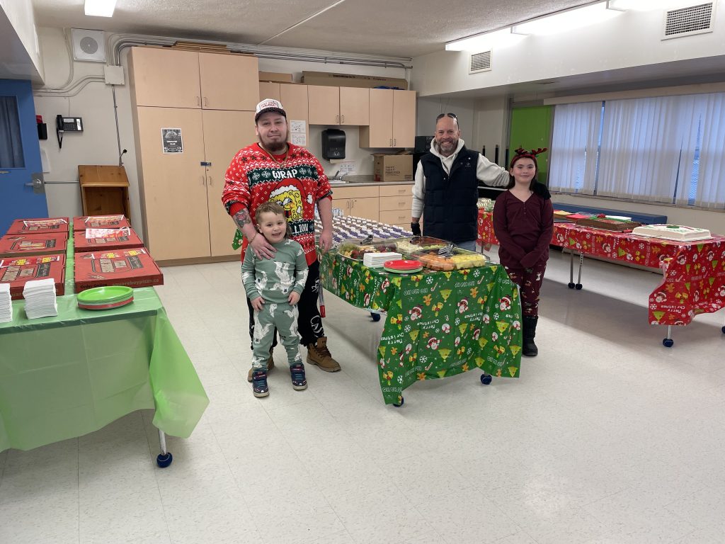 Two men and two children stand around a table of donated food for a Christmas lunch at a school.