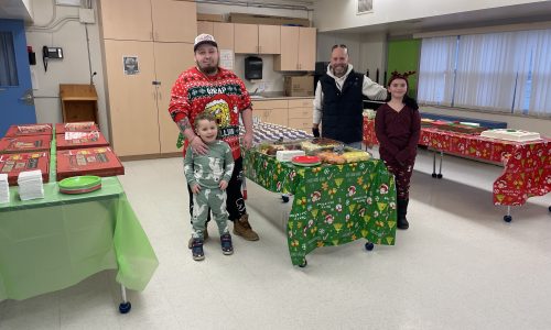 Two men and two children stand around a table of donated food for a Christmas lunch at a school.