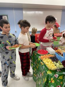 Three boys in pajamas line up to get food at a Christmas lunch at a school