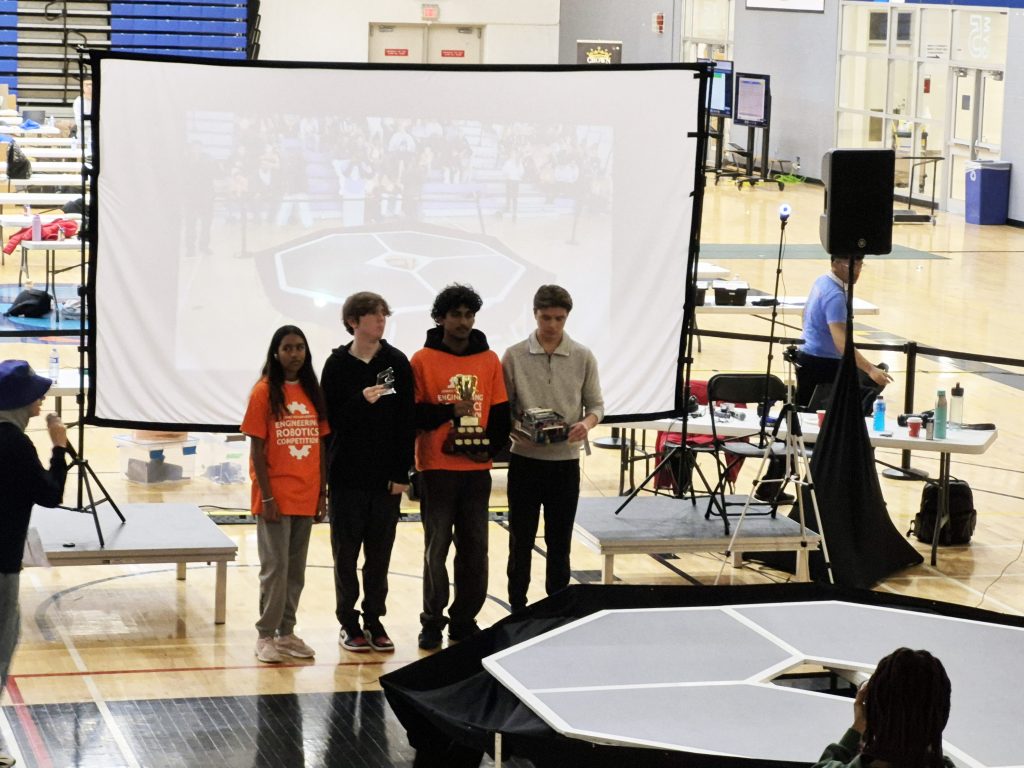 Four students pose with a trophy at a robotics competition.