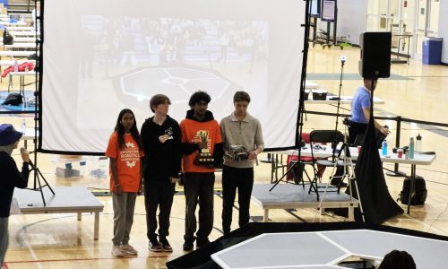Four students pose with a trophy at a robotics competition.