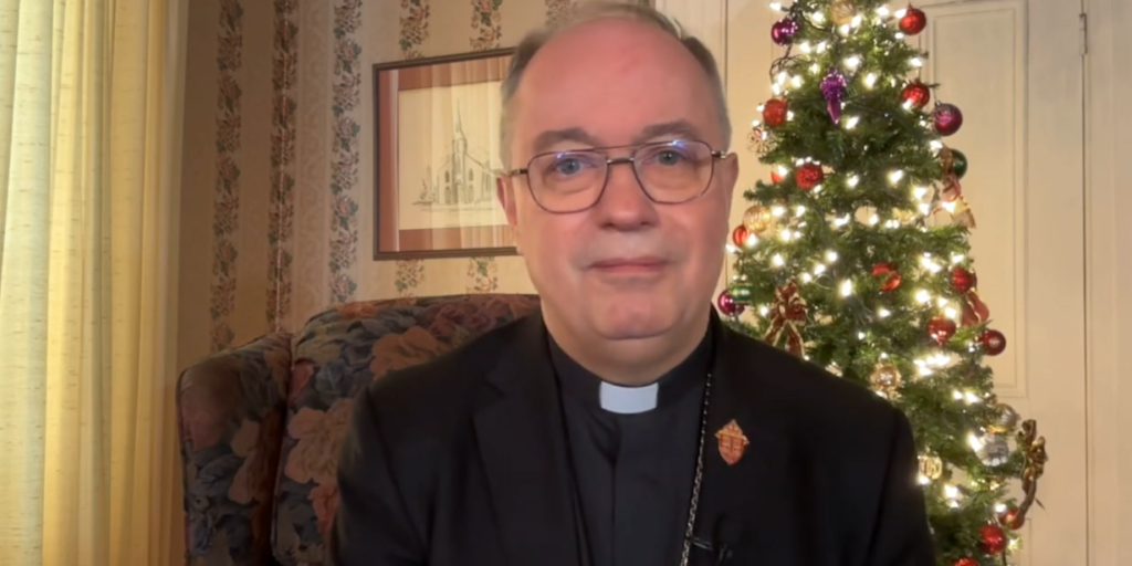 Bishop Daniel Miehm sits in front of a Christmas Tree to deliver his Christmas message.