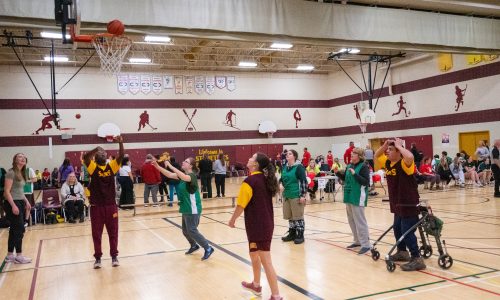Student athletes play basketball in a school gym for a Special Olympics qualifier event.