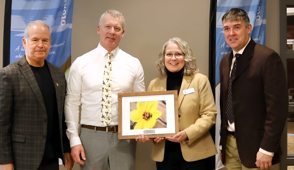 Four adults stand with a framed photo of a flower at an awards ceremony.