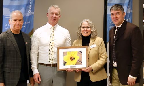 Four adults stand with a framed photo of a flower at an awards ceremony.