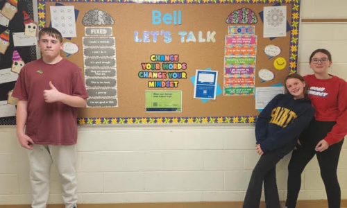 Three students stand in-front of a decorative bulletin board for a photo.