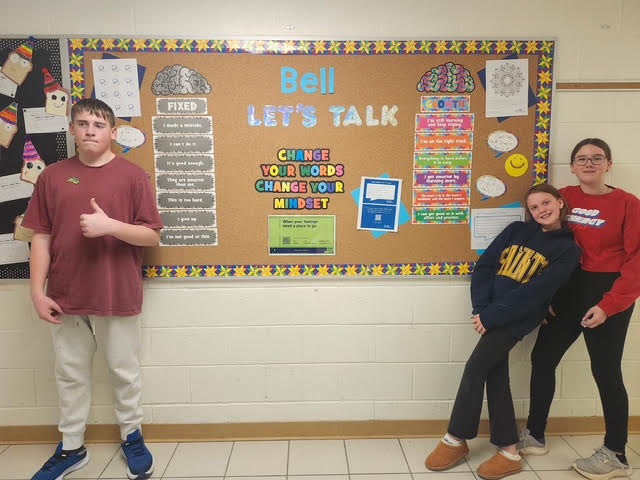 Three students stand in-front of a decorative bulletin board for a photo.