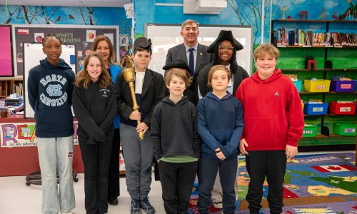 Students pose with the Speaker of the Ontario Legislative Assembly and the local Member of Provincial Parliament during a presentation at a school.