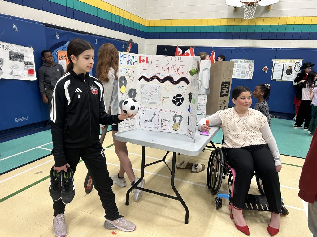 Two students stand by a project board in a gym.
