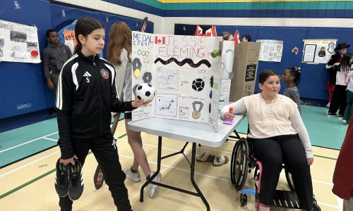 Two students stand by a project board in a gym.