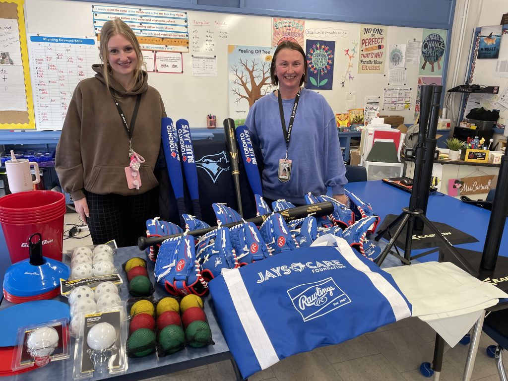 Two adults stand around several pieces of baseball equipment.