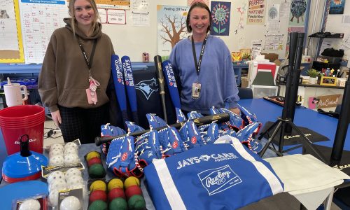 Two adults stand around several pieces of baseball equipment.