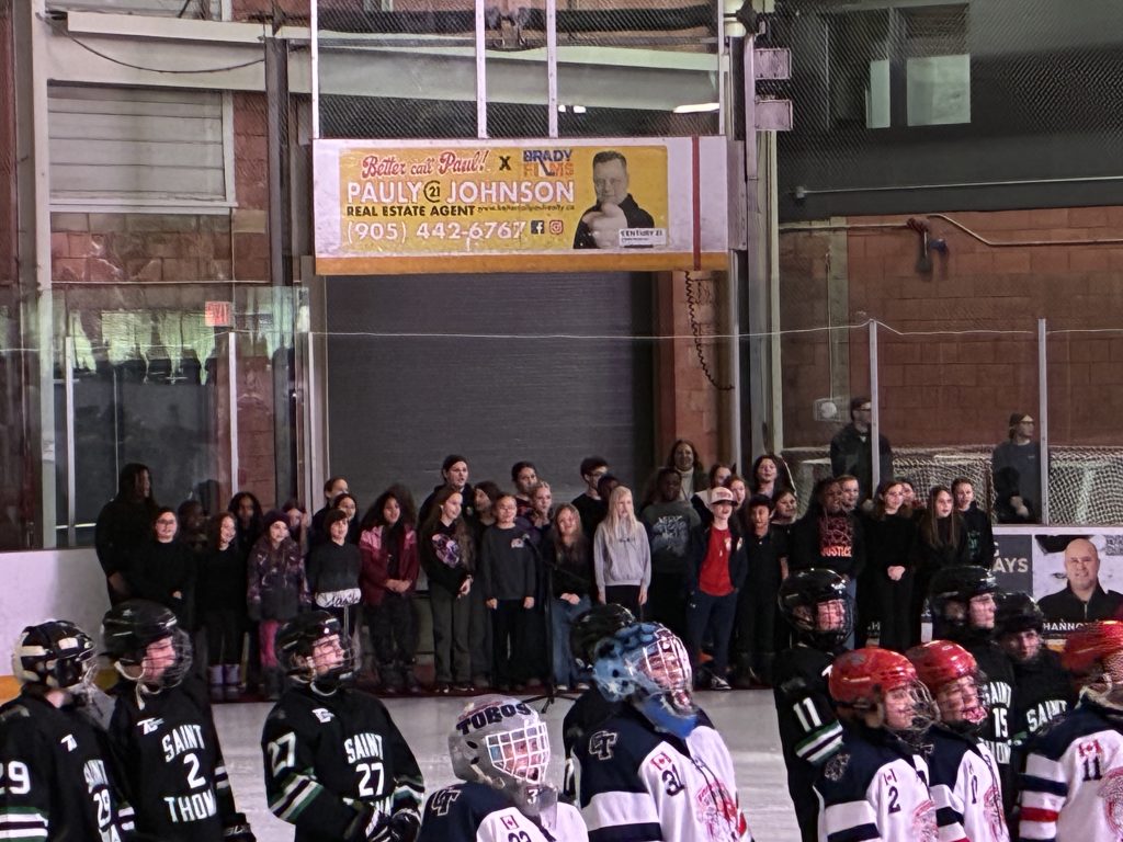 A choir of students performs O Canada at a hockey tournament.
