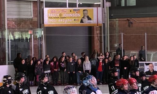 A choir of students performs O Canada at a hockey tournament.