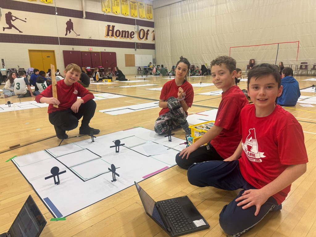 Four students wearing red t-shirts participate in a robotics competition featuring LEGO.