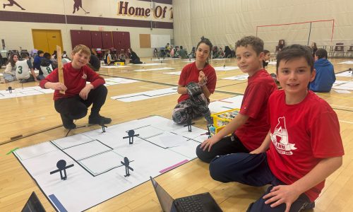 Four students wearing red t-shirts participate in a robotics competition featuring LEGO.