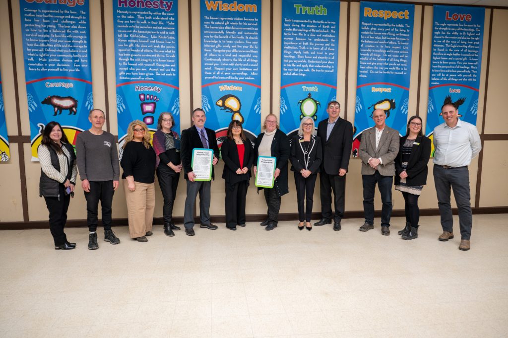 A group of adults poses at a funding announcement at a community centre.
