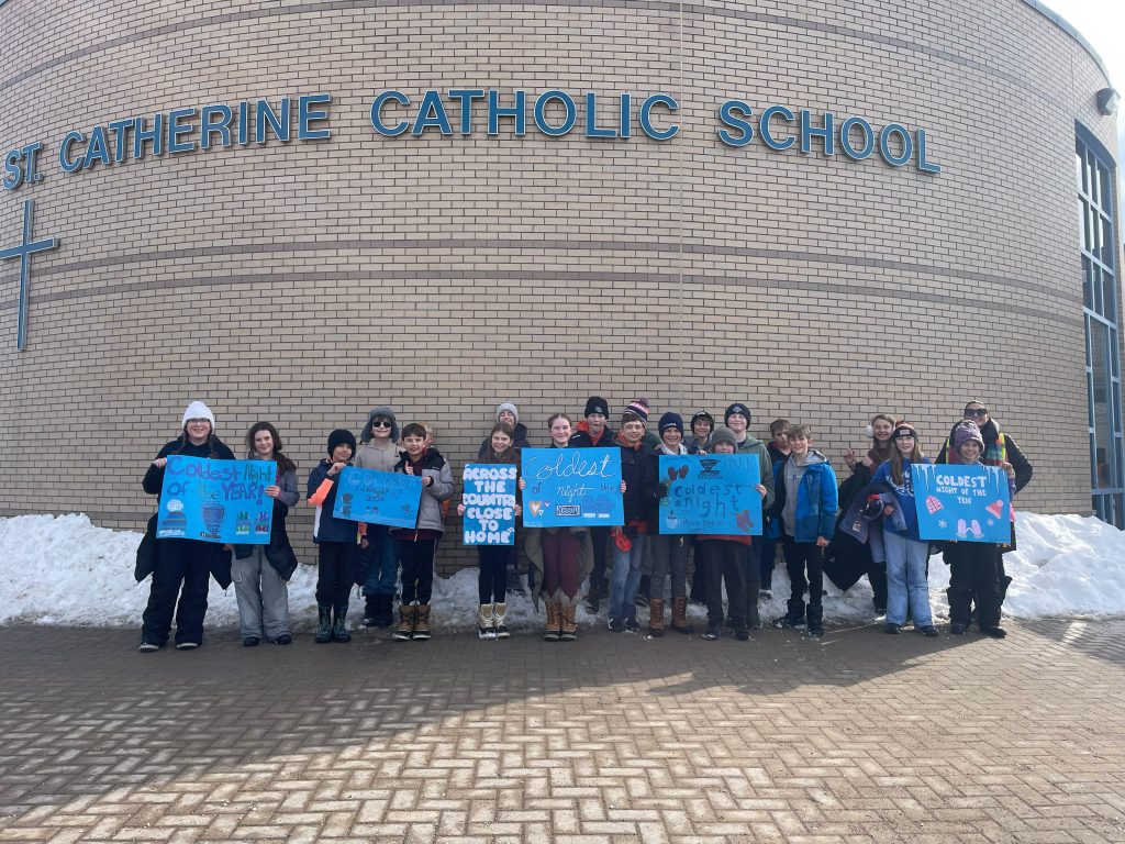 Students holding blue signs stand outside of a school on a winter day.