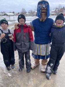Three students stand with a mascot at a winter carnival.