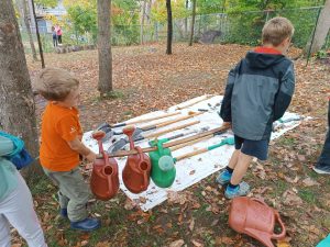 Two students carry watering cans in a forest.